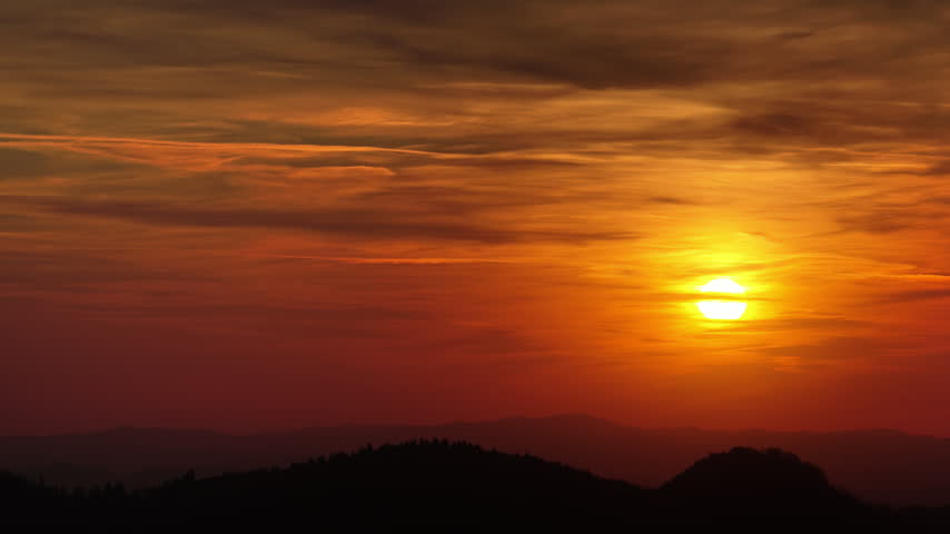 Aerial drone view of the sky glowing orange over darkened hills, in Romania, at dusk