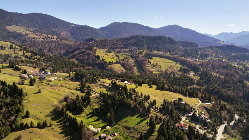 Aerial drone view of green hills, scattered houses, and forest patches in the Bucovina region near Vatra Dornei, Romania