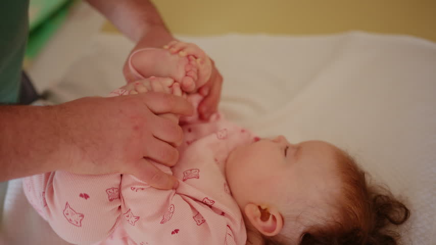 Baby lying on a padded treatment table while an adult gently supports the legs during a pediatric movement exercise