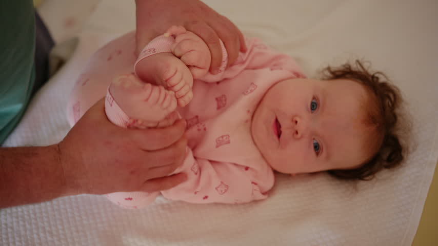 Baby lying on a padded treatment table while an adult gently supports the legs during a pediatric movement exercise