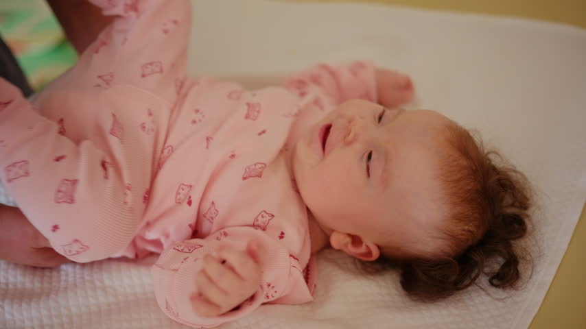 Baby lying on a padded treatment table while an adult gently supports the legs during a pediatric movement exercise