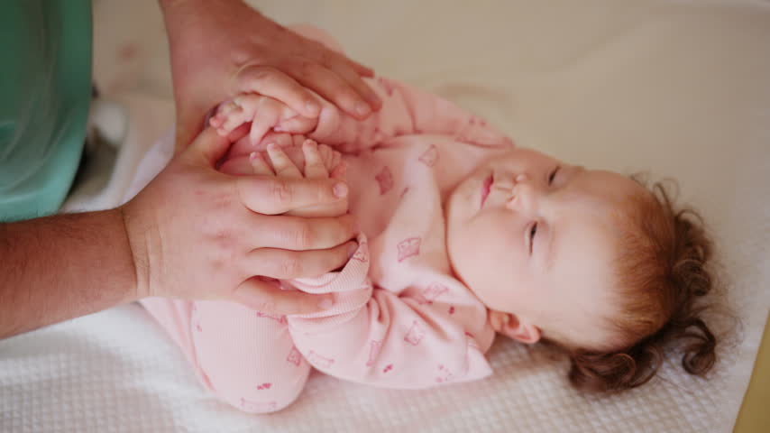 Baby lying on a padded treatment table while an adult gently supports the legs during a pediatric movement exercise