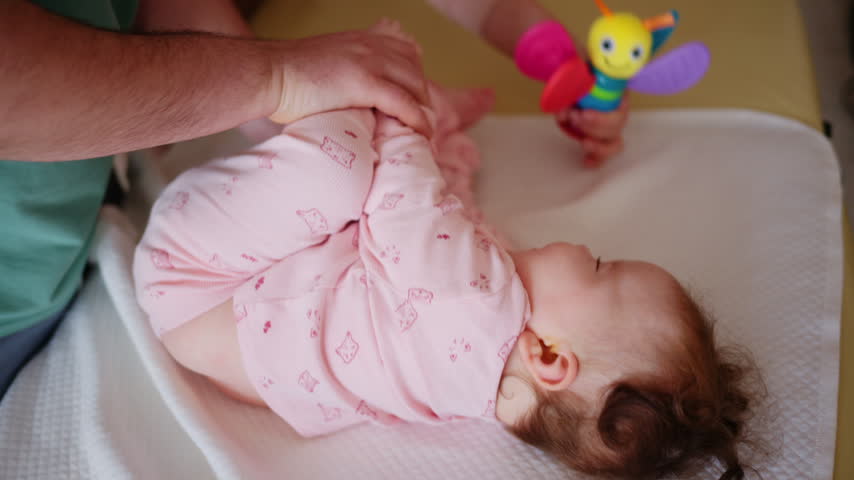 Baby lying on a padded treatment table while an adult gently supports the legs during a pediatric movement exercise