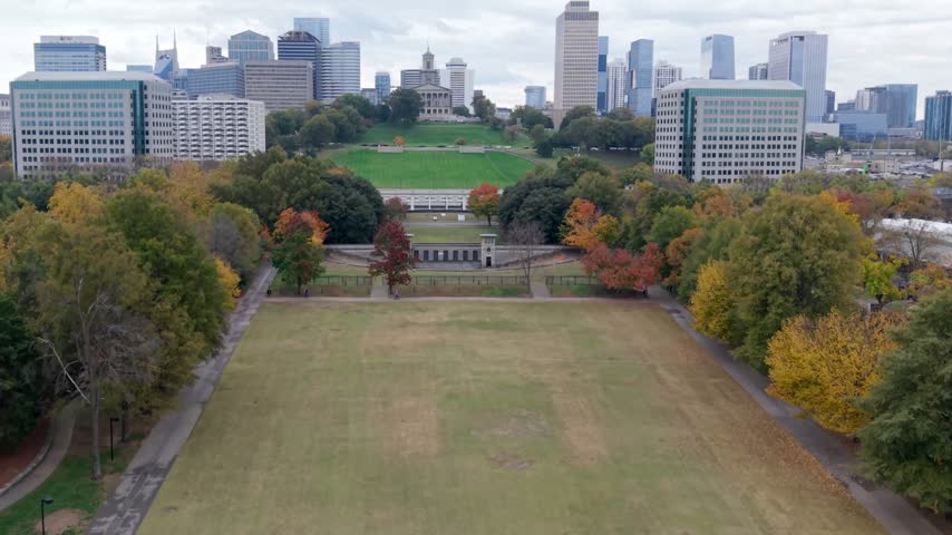 Autumn color fills Bicentennial Capitol Mall State Park below the Tennessee State Capitol in Nashville, the downtown skyline rising beyond the open lawns. Aerial rising shot