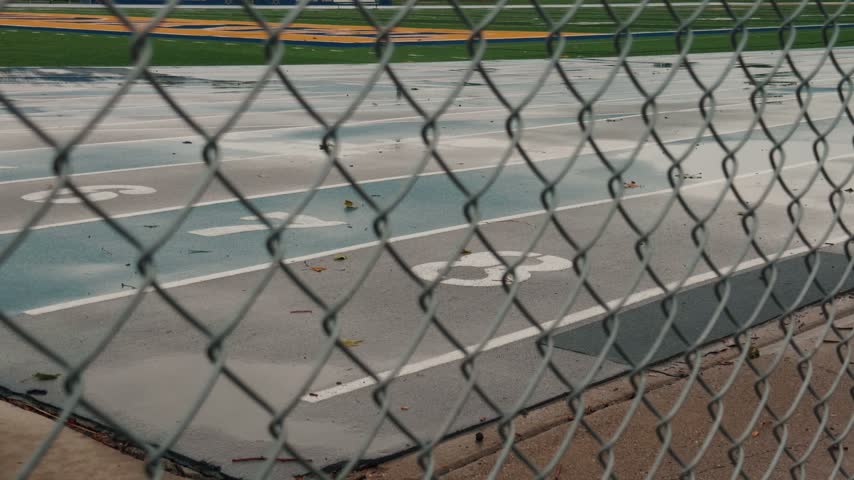 Still shot of a wet running track viewed through a chain link fence