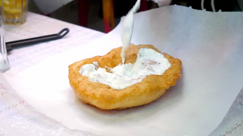 At Szimpla Kert market, a womans hands carefully season the traditional Krumplis Langos with sour cream and grated cheese, a beloved Hungarian street food.