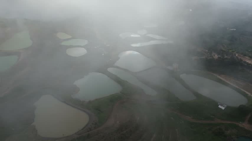 An aerial drone shot overlooking the artificial ponds of Qornayel Lakes in Lebanon, partially obscured by low-hanging fog and clouds.