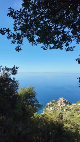Coastal village on a rocky promontory framed by trees. Corniglia, Cinque Terre, Italy.