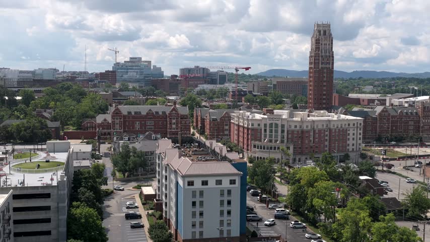 West End Tower rises in collegiate Gothic brick over the Vanderbilt University campus in Nashville, Tennessee, apartment blocks and construction cranes around it. Aerial drone wide shot