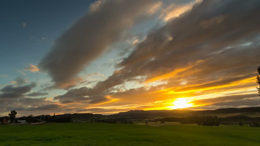 Timelapse of dramatic clouds over green farmland at sunset, Norway