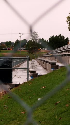 Static vertical view of wet concrete bleachers through an out-of-focus chain-link fence.