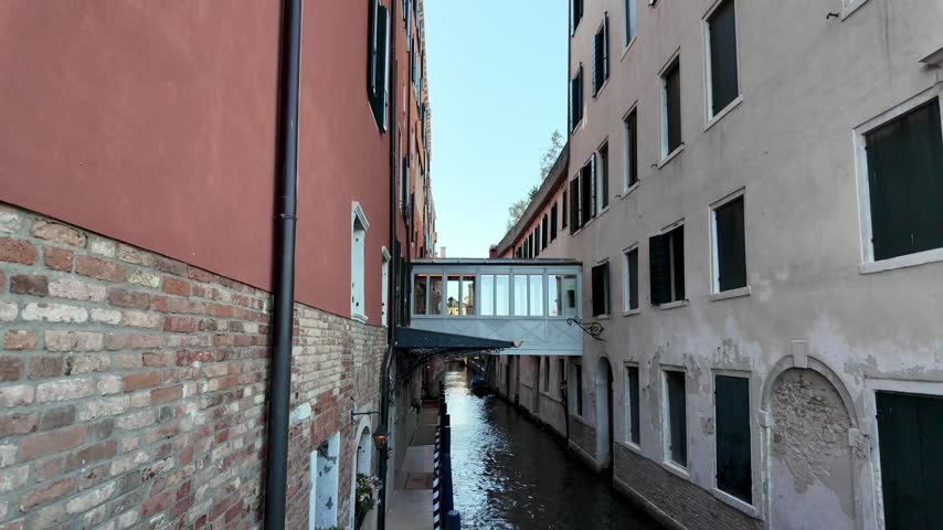 Narrow canal in Venice surrounded by historic buildings, small bridges, restaurants and colorful waterfront facades
