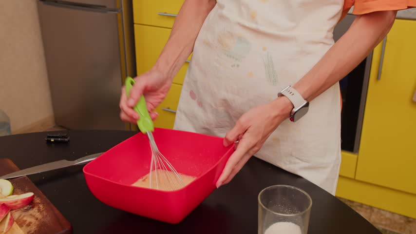Close-up of woman mixing batter with whisk in home kitchen. Preparing homemade food by hand