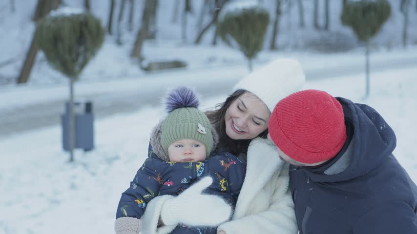 Young happy family with a baby enjoying a walk in a snowy park. Loving parents playing with their infant child outdoors in winter