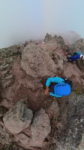 High angle view of mountaineers ascending a steep, rocky trail on a foggy day on a volcano