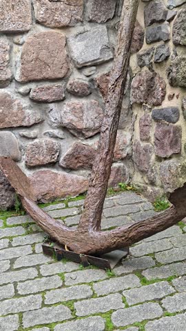 A large anchor sits on top of a brick sidewalk.