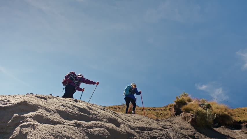 Determined hikers ascending a steep, sandy trail on a sunny day with clear blue skies