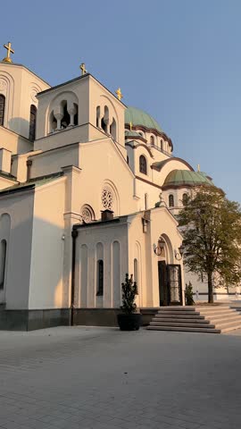 Belgrade, Serbia. Vertical street city video with zoom effect. Majestic Church of Saint Sava with white facade, green domes, crosses. Clear blue sky during golden hour sunset lighting