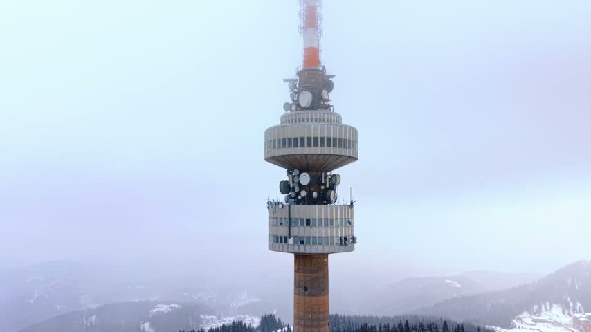 Concrete telecommunication tower in winter mist. Antenna dishes and circular platforms sit on a tall transmitter shaft during foggy weather.