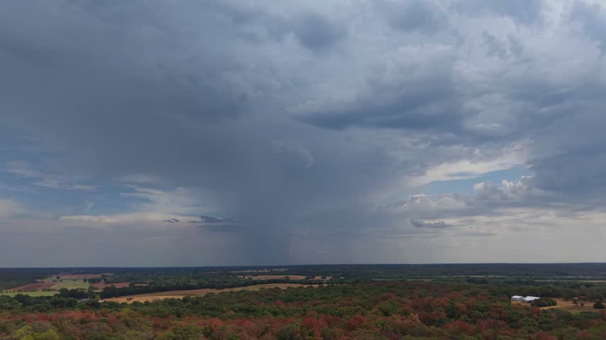 Autumn forest foliage with a dark rain cloud approaching over rural Oklahoma countryside in a forward tracking aerial shot.