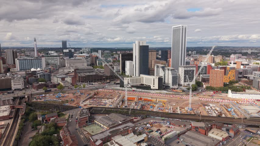 Aerial view across railway tracks and a large construction site with tower cranes, revealing modern high-rise buildings and the evolving skyline of Birmingham, England.