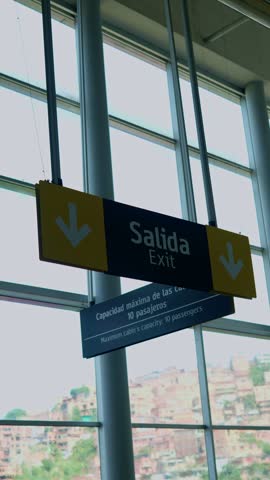 Spanish and english exit sign hanging in a modern station with the cityscape of medellin visible outside