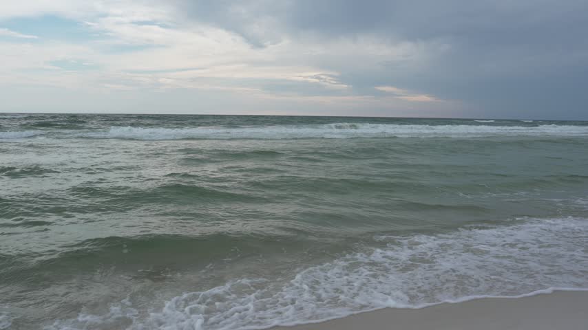 Choppy ocean waves and cloudy sky on a Florida beach, stormy weather. Video footage of rough ocean waves rolling onto a sandy beach shore under a moody overcast sky, stormy weather and coastal nature concept.