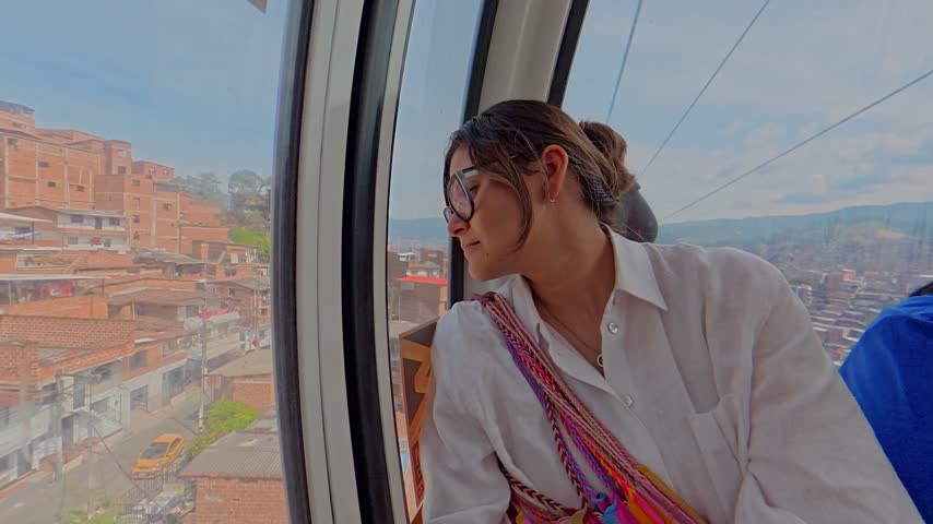 Young woman tourist on a metrocable car looking at the cityscape of medellin, colombia from above