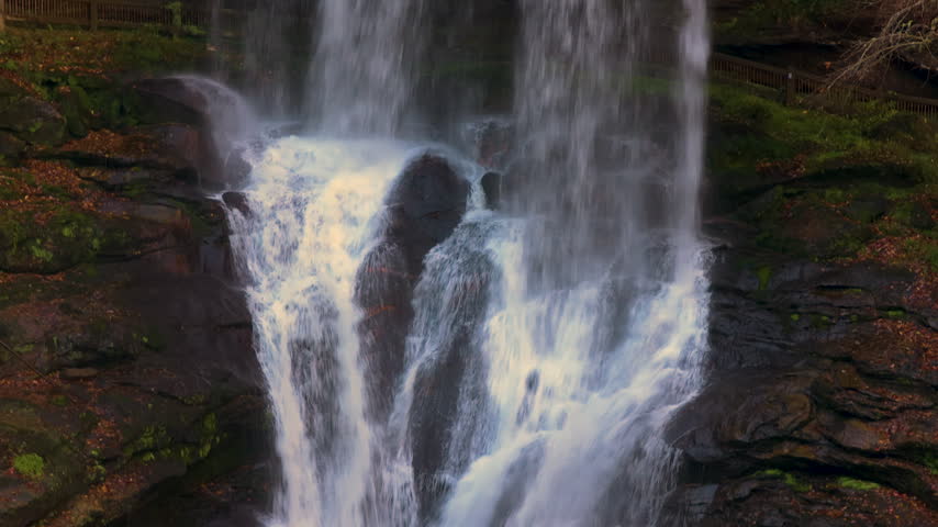Scenic waterfall with clear water cascading over rocky ledge surrounded by golden autumn forest.