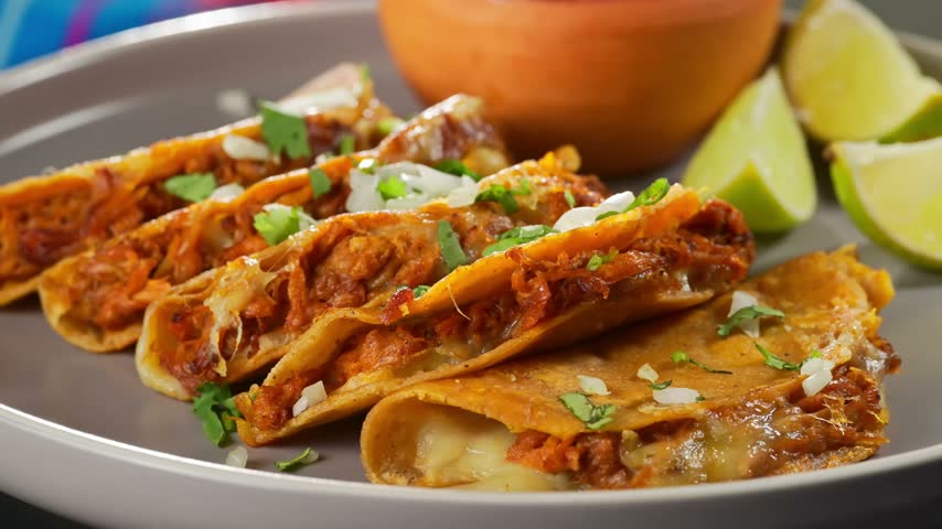 Delicious beef birria tacos with melted cheese, chopped onions, cilantro and fresh lime wedges served on a plate