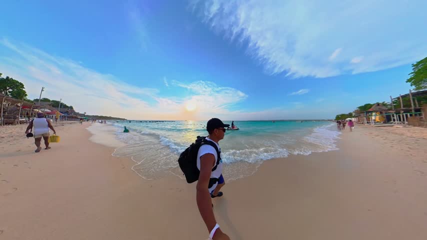 Young man holding a selfie stick walking along the shoreline of a beautiful caribbean beach in colombia