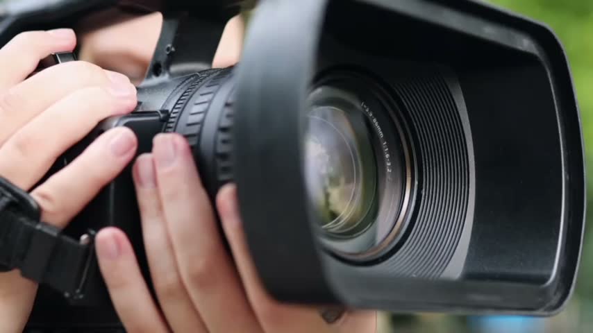 Extreme close-up of a professional camera lens with visible glass elements and reflections, creating a detailed cinematic view of photography and optical technology.