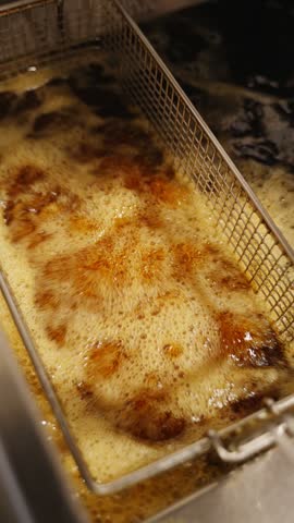 Close-up of crispy fried chicken wings with a golden coating in a metal fryer basket in a restaurant kitchen.