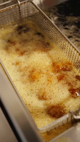 Close-up of crispy fried chicken wings with a golden coating in a metal fryer basket in a restaurant kitchen.