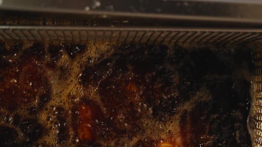 Close-up of crispy fried chicken wings with a golden coating in a metal fryer basket in a restaurant kitchen.