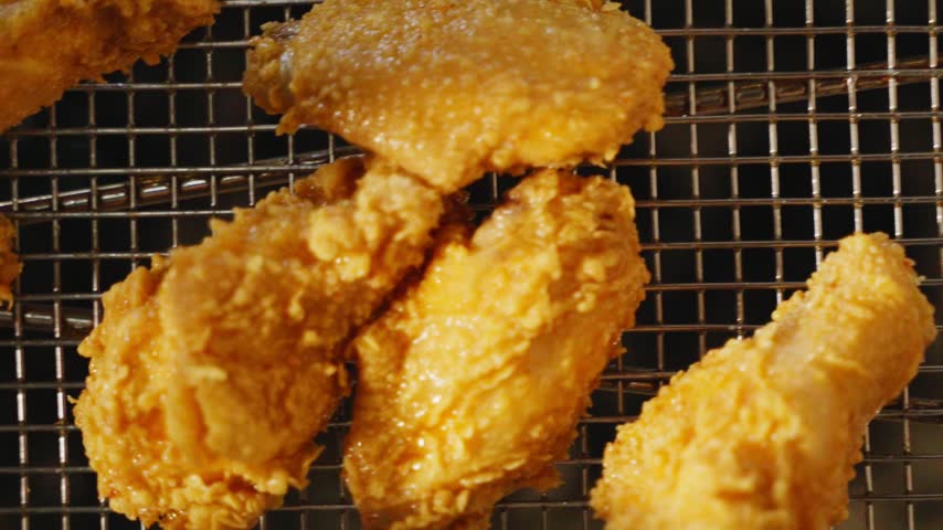 Close-up of crispy fried chicken wings with a golden coating in a metal fryer basket in a restaurant kitchen.