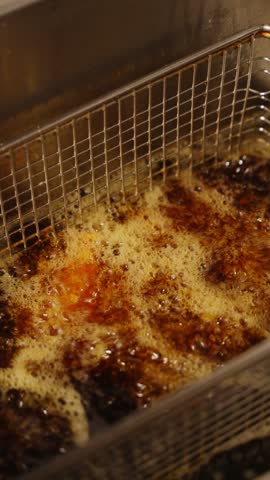 Close-up of crispy fried chicken wings with a golden coating in a metal fryer basket in a restaurant kitchen.