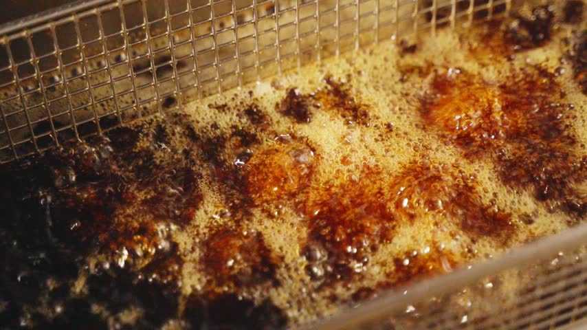Close-up of crispy fried chicken wings with a golden coating in a metal fryer basket in a restaurant kitchen.