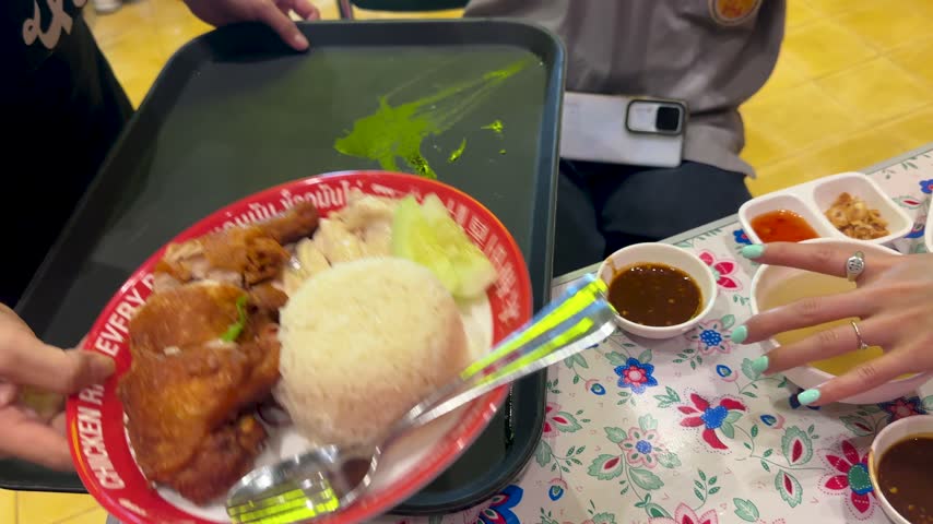 Close-up of crispy fried chicken with white rice and cucumber on a floral table.
