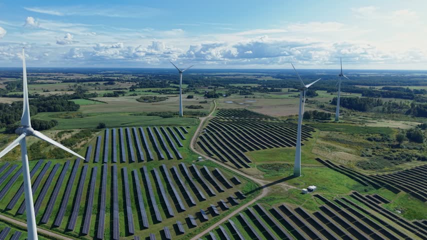 Stunning aerial footage showcases wind turbines and rows of solar panels generating clean energy across a vast farmland under bright daylight with dynamic cloud cover.