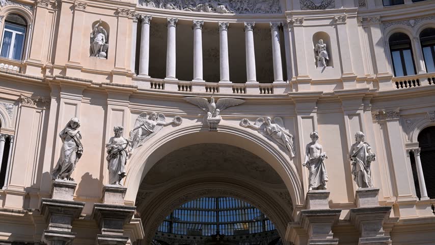 Classical marble statues and ornate reliefs frame the main entrance arch of Galleria Umberto I in Naples under bright daylight.
