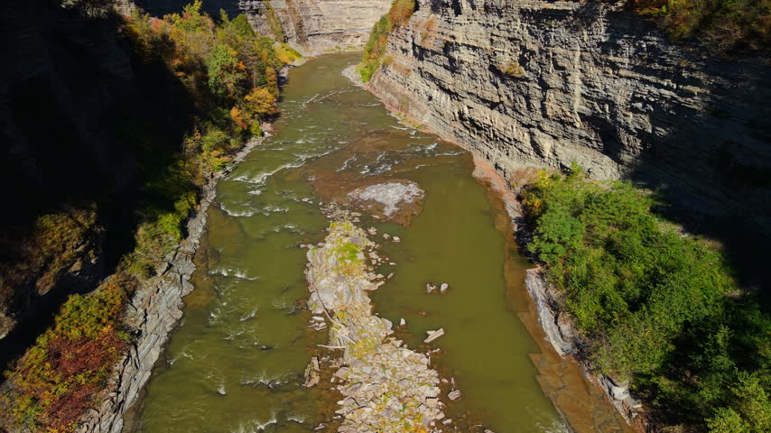 Autumn foliage surrounds a rocky canyon and flowing river in Letchworth State Park, New York, USA.