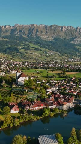 Vertical aerial view of Werdenberg, Switzerland, with Lake Werdenberg, medieval timber houses, vineyards and the dramatic Churfirsten mountains across the Rhine Valley.