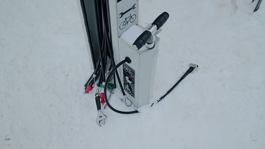 Public bicycle repair tools and air pump stand surrounded by winter snow