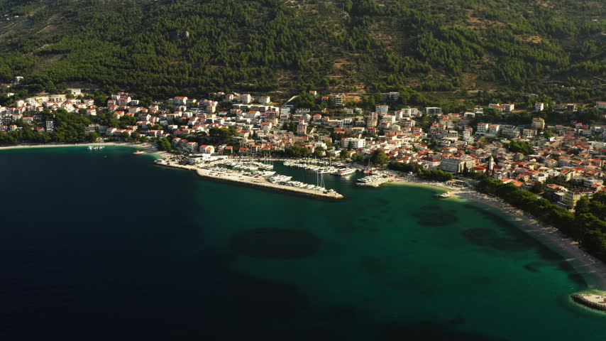 A central marina harbor docks yachts in the resort town of Baska Voda, Croatia. Sunny pebble beaches and holiday houses surround the port along the Adriatic Sea for summer vacation travel.