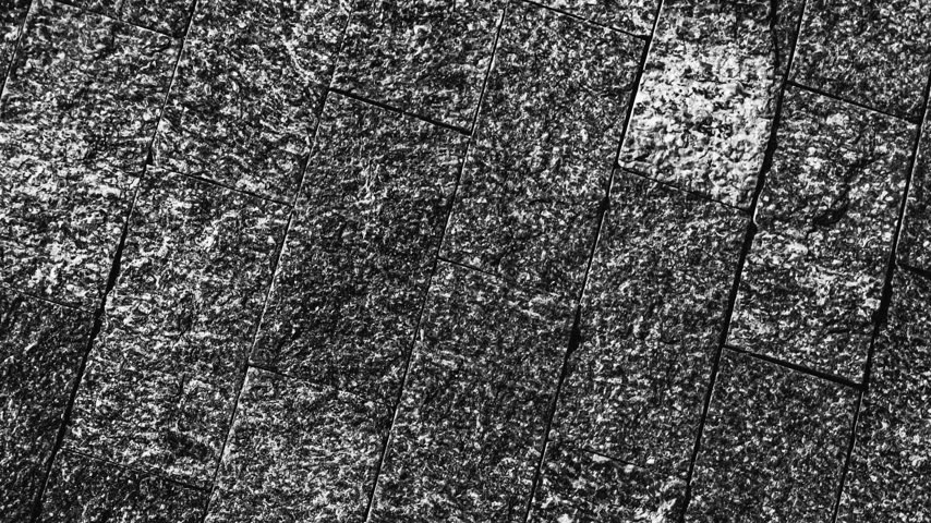 Detailed close-up of a rough, dark grey granite stone surface exhibiting a linear pattern and granular texture, ideal for construction or design backgrounds.