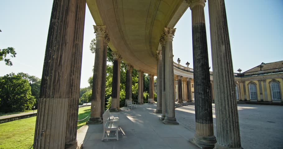 Sanssouci Palace colonnade in Potsdam, Germany, with a shaded walkway, stone columns and views into the courtyard.