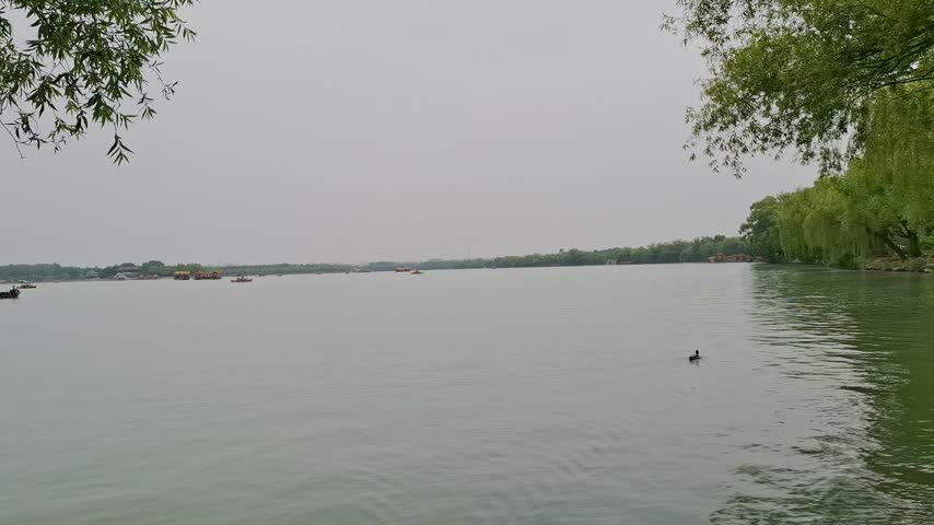 Scenic view of calm Kunming Lake with traditional boats at the Summer Palace under an overcast sky, historic Chinese architecture and tourism in Beijing, China.