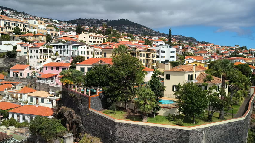Panoramic view of colorful hillside houses, lush gardens under a bright blue sky in Funchal, Madeira, Portugal.