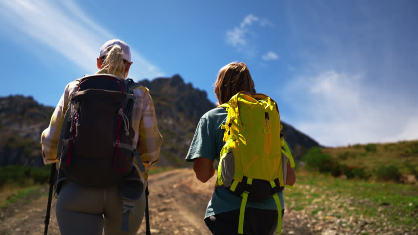 Young boy pointing to a mountain peak while hiking with his mother on a scenic trail. Couple of travelers with backpacks enjoying an active vacation and exploring nature together